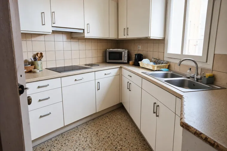 Antes del cambio: cocina blanca con encimera de laminado beige desgastada, azulejo pequeño y fregadero antiguo (recreación ilustrativa)