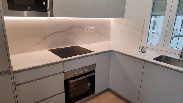 Cocina en L con encimera y frente de porcelánico Ascale Torano Oro mate, muebles blancos y luz led: encimera montada por Kitchenmania
