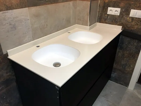 Mueble de baño negro con encimera blanca de dos lavabos integrados sobre paredes de piedra: baño montado por Kitchenmania en Madrid