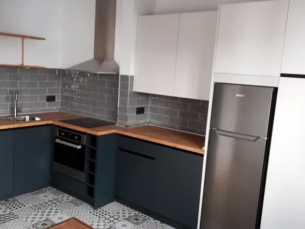 Cocina con muebles bajos azul oscuro, altos blancos, encimera de roble, azulejo metro gris y suelo hidráulico: cocina montada por Kitchenmania