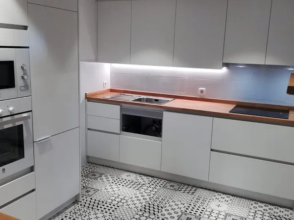 Cocina blanca sin tiradores con encimera de madera, columna de horno y microondas y suelo de baldosa hidráulica: cocina montada por Kitchenmania