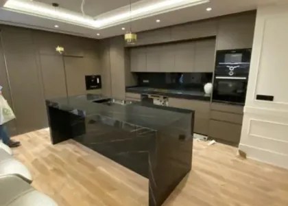 Cocina en tono gris topo con isla de piedra negra veteada, horno en columna y luz indirecta en el techo: cocina montada por Kitchenmania